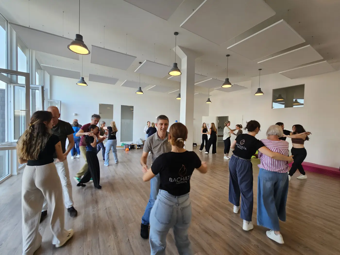 Paare üben eine Figur im Kursraum, eine Tänzerin trägt das Bachata-Viersen-Shirt